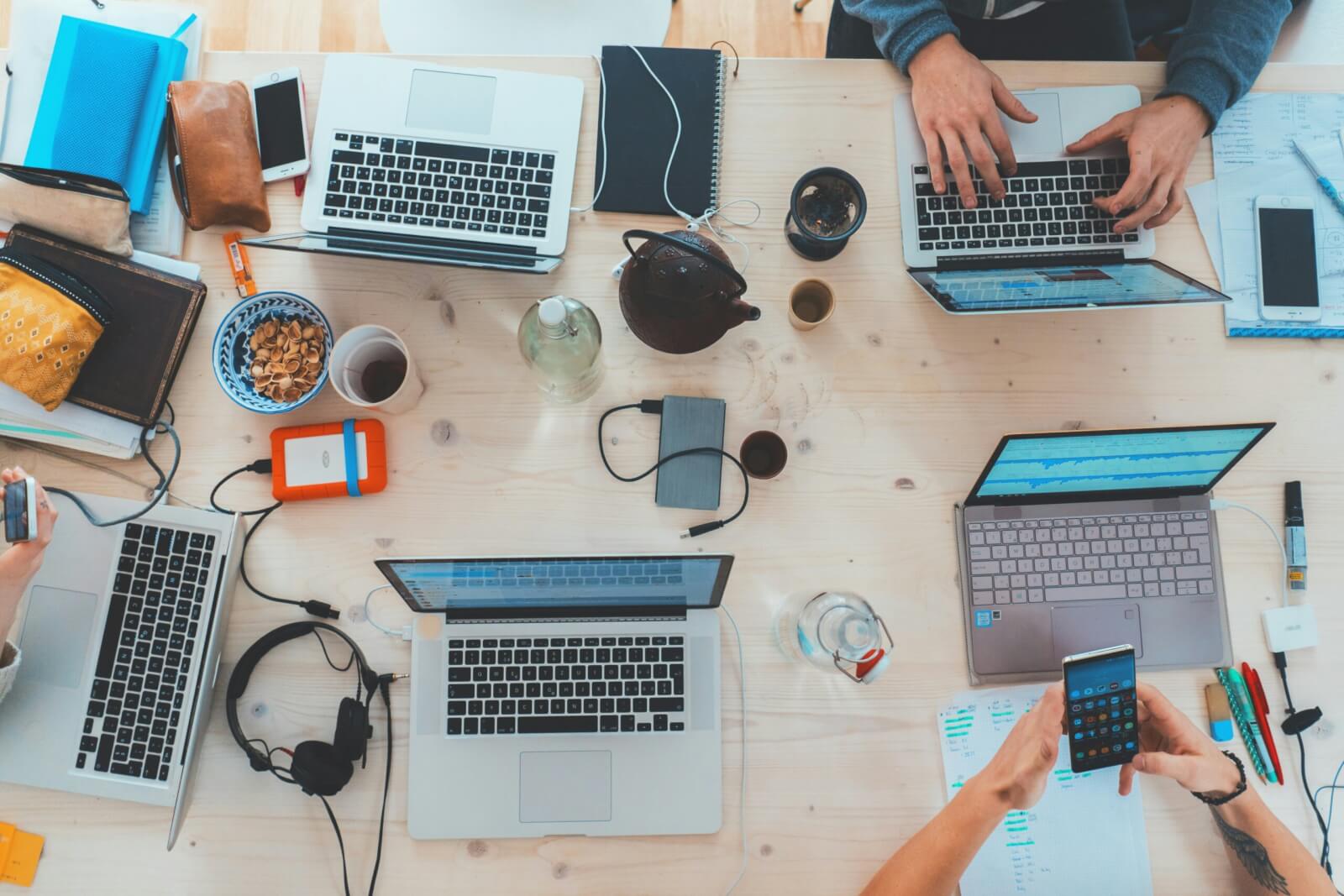 A group of computers on a table with people typing on them.